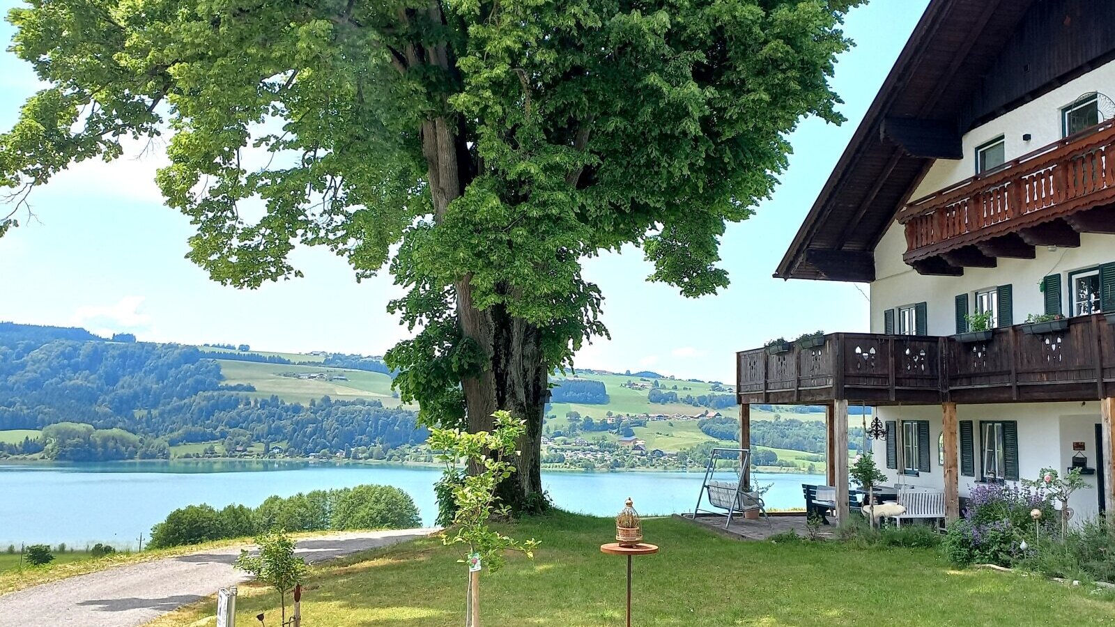 The Farm House features balconies and a garden with an outdoor seating area, offering views of the lake and forested hills.