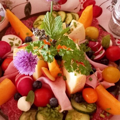 A farm house breakfast platter featuring an assortment of cheeses, cold cuts, radishes, tomatoes, cucumbers, and berries.