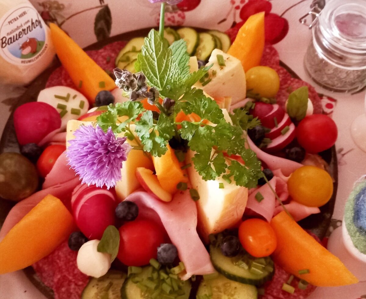 A farm house breakfast platter featuring an assortment of cheeses, cold cuts, radishes, tomatoes, cucumbers, and berries.