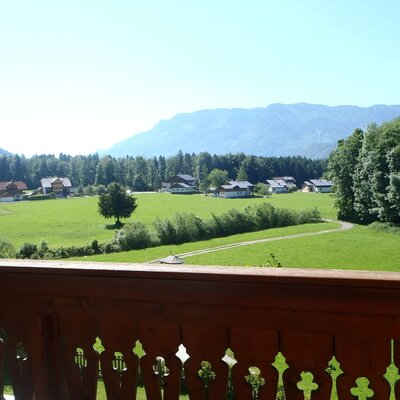 Balcony view from the Farm House, featuring green countryside, distant houses, and mountains.