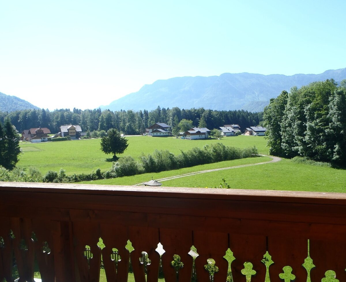 Balcony view from the Farm House, featuring green countryside, distant houses, and mountains.