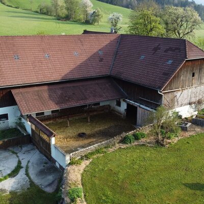 The main building of Biohof Grubbauer with a red tiled roof and an adjacent animal enclosure.