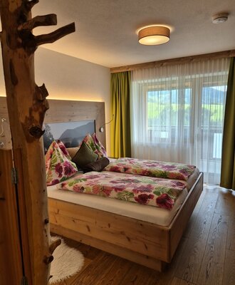 Double bedroom in the farm house featuring a natural wood bed frame, floral duvets, and a large window with views of green fields.