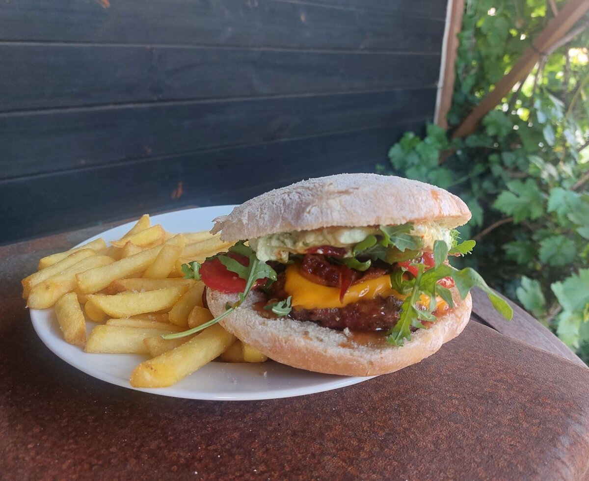 A burger with a patty, cheese, rocket, and tomato, served with a side of french fries at the farmhouse.