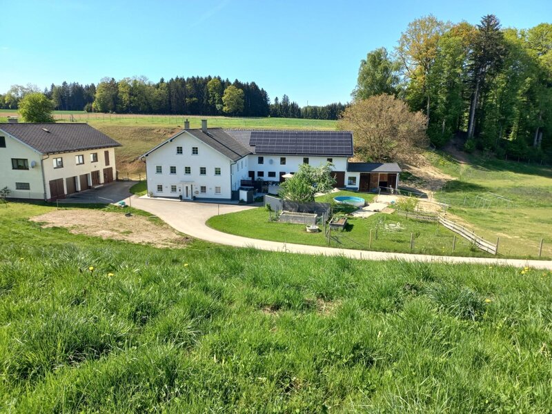 Exterior view of the Bed and Breakfast with a driveway, lawn, small pool, and surrounding fields and forest.