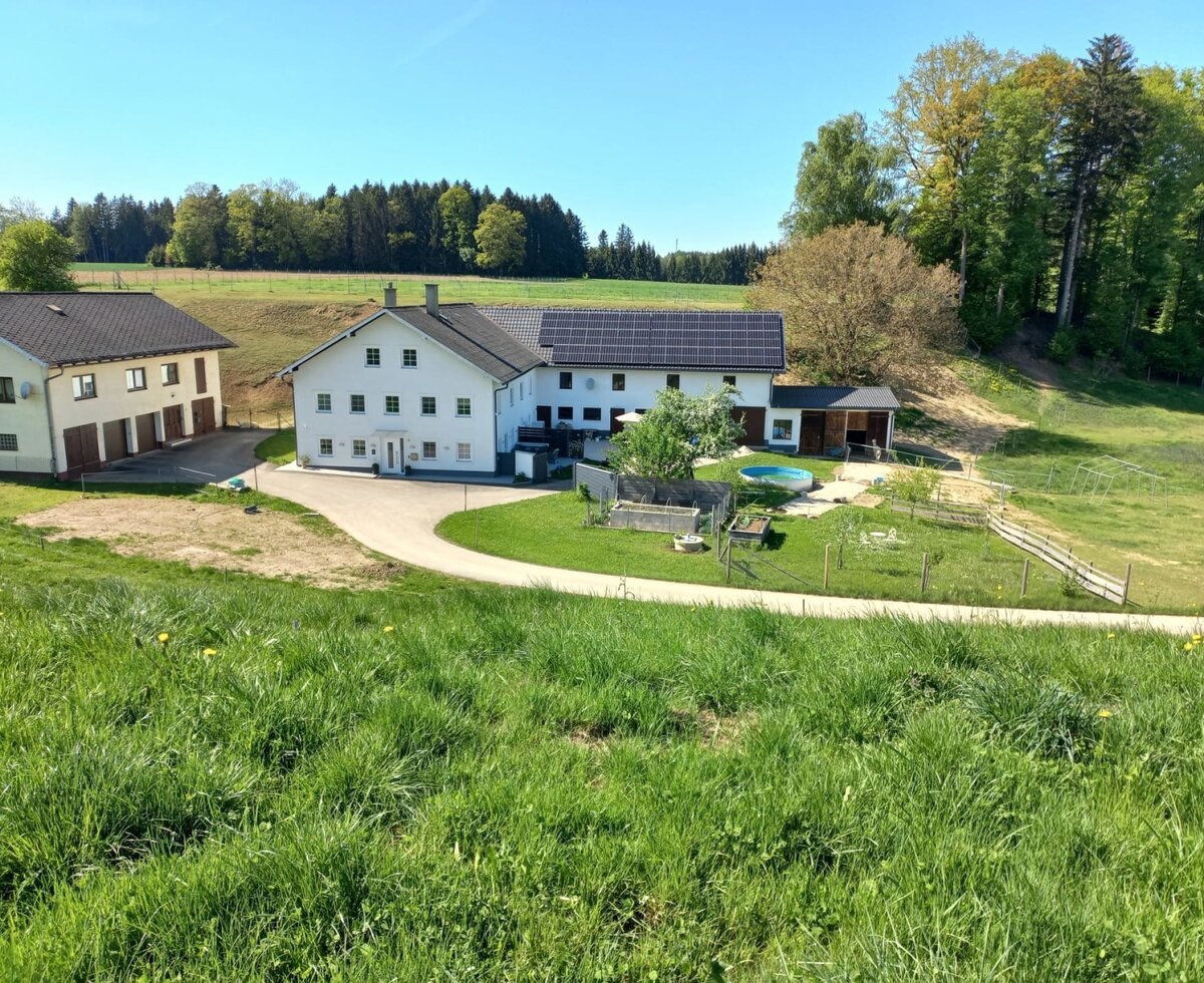 Exterior view of the Bed and Breakfast with a driveway, lawn, small pool, and surrounding fields and forest.