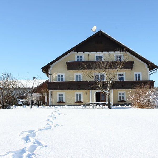 The Farm House exterior in winter, featuring multiple balconies and a snow-covered yard with a swing set.