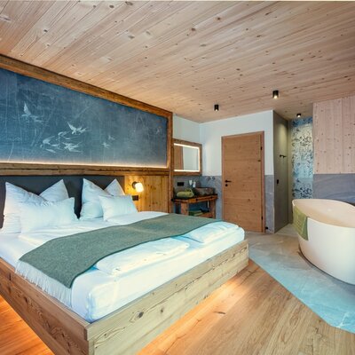 Double bed in the chalet with a freestanding bathtub, wooden elements, and a wall-mounted TV.