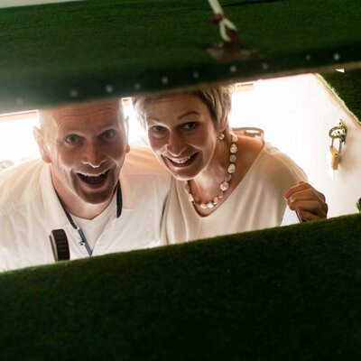 Two guests smiling from a uniquely designed bed featuring a green, grass-like interior in a holiday apartment at the Farm House.