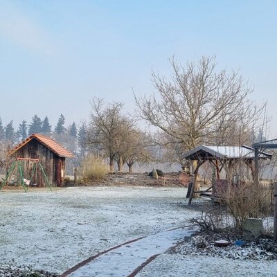 The frost-dusted garden at the farmhouse, equipped with a wooden shed, a swing set, and a covered seating area.