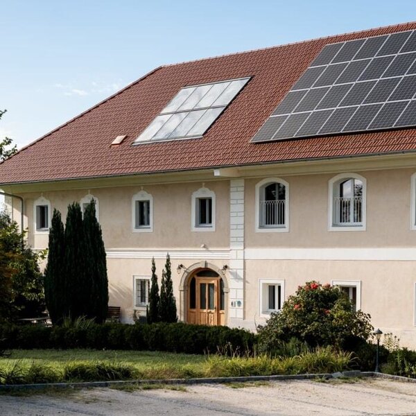 The inviting farmhouse building featuring a well-kept green garden and modern solar panels on the roof.