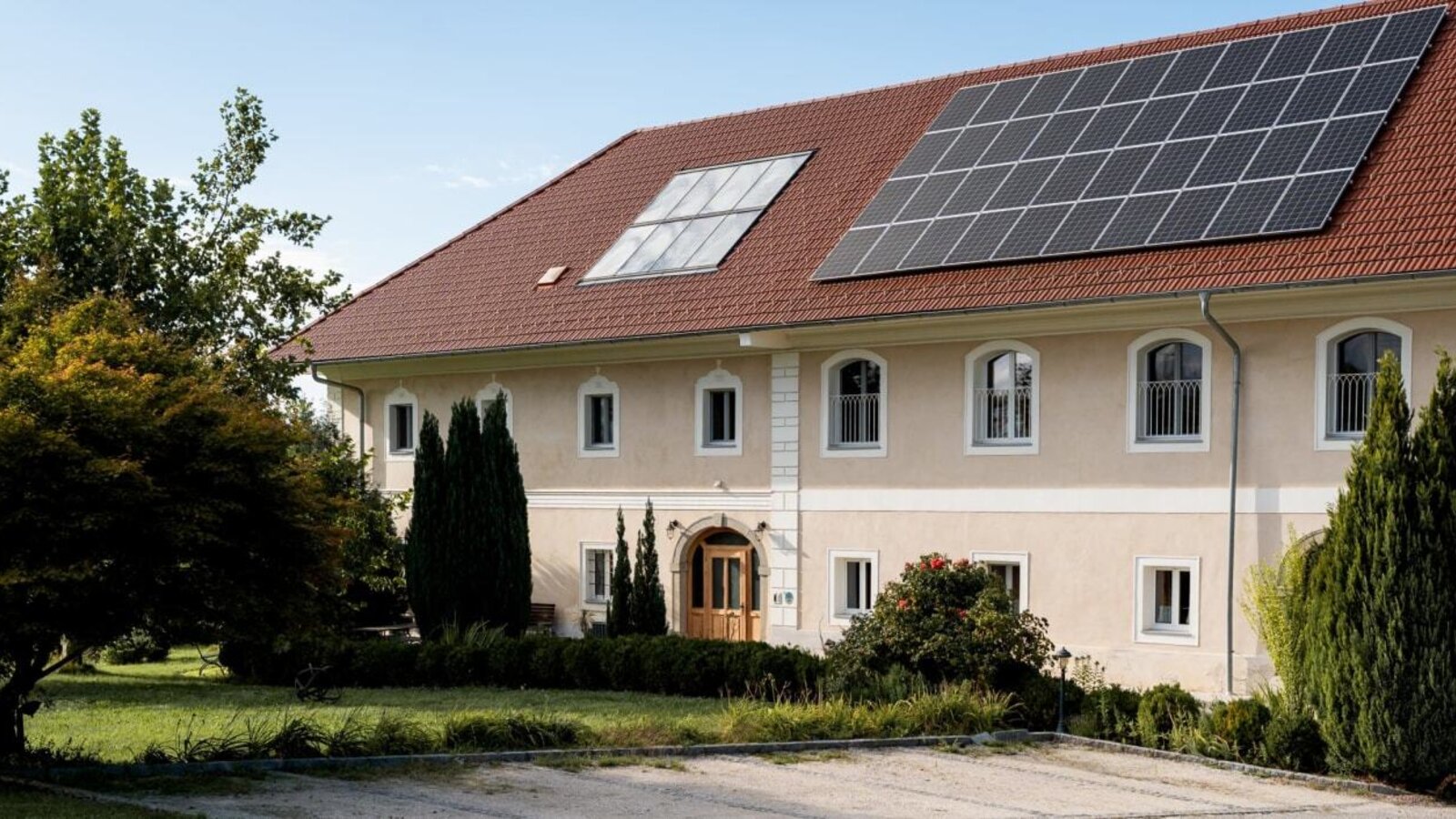 The inviting farmhouse building featuring a well-kept green garden and modern solar panels on the roof.