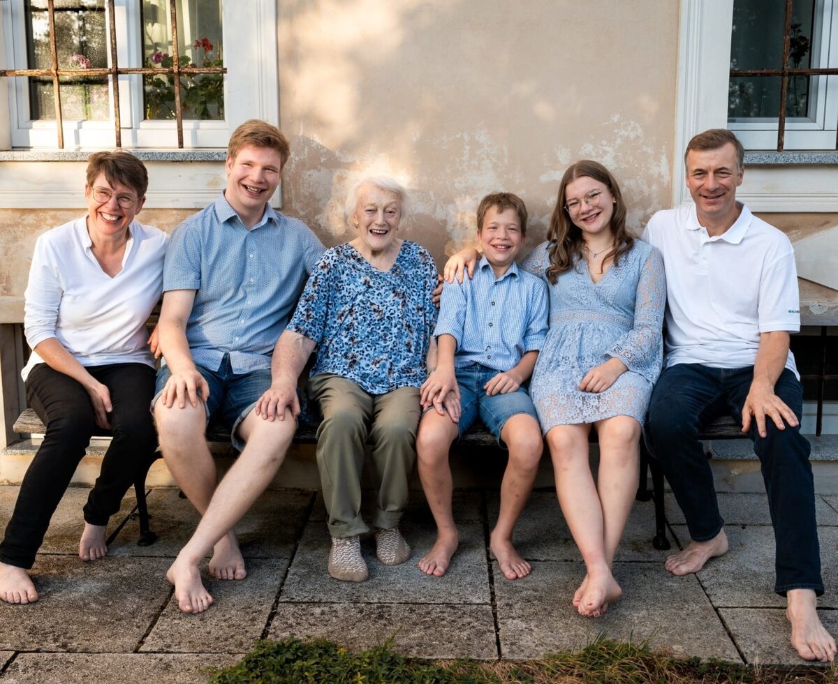 The welcoming host family sitting together on a cozy wooden bench in front of the farmhouse.