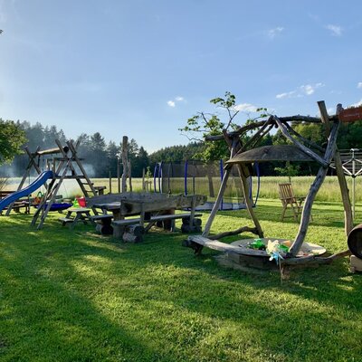 The farmhouse's spacious garden featuring an inviting children's playground with a slide, trampoline, and rustic wooden seating.