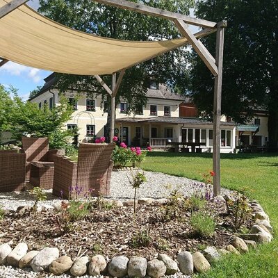 Outdoor seating area of the farmhouse with a pergola, sunshade, and wicker chairs, surrounded by garden and lawn.