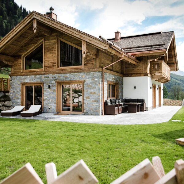 The inviting holiday home featuring a lush green lawn and a spacious stone terrace set against a scenic mountain backdrop.