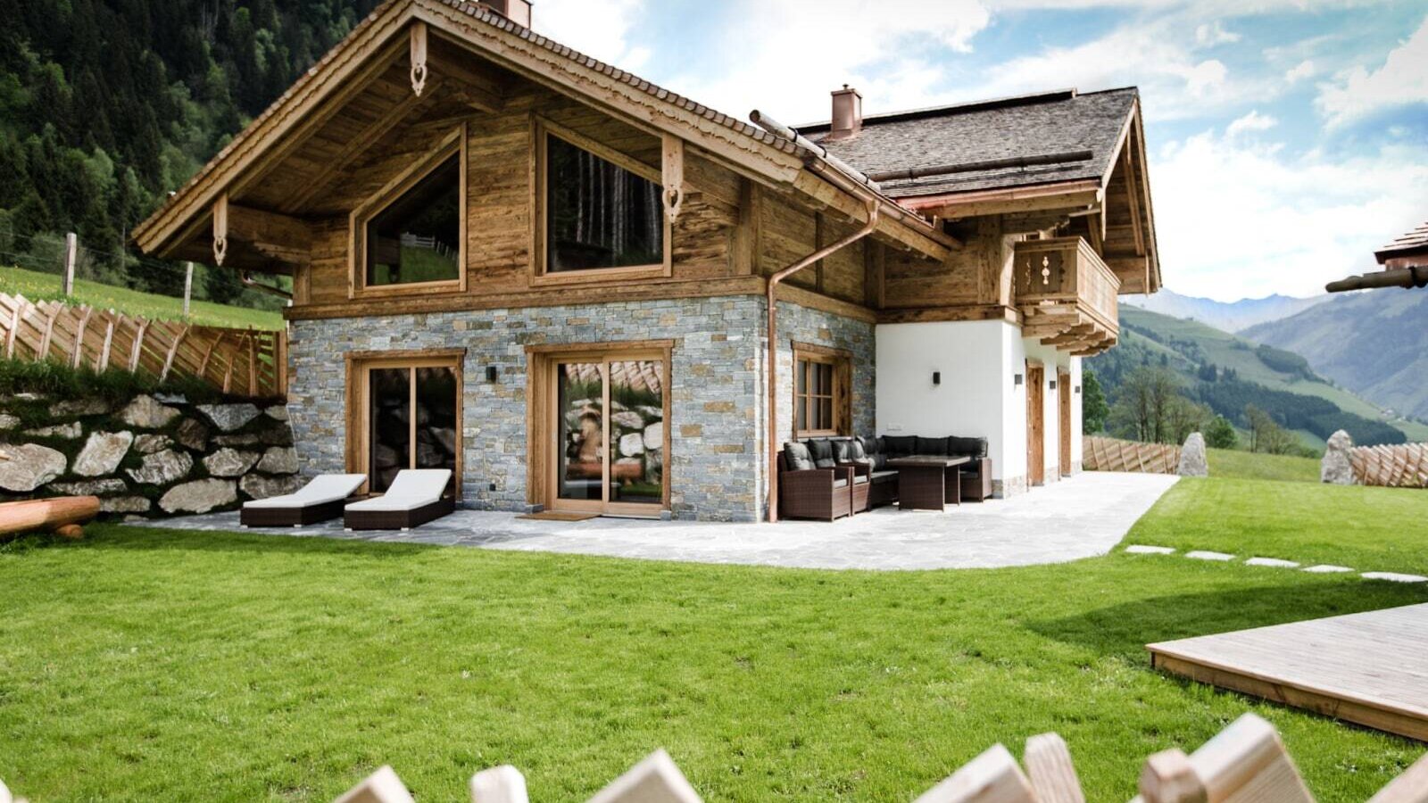 The inviting holiday home featuring a lush green lawn and a spacious stone terrace set against a scenic mountain backdrop.