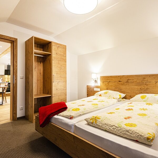 Bedroom in the Farm House featuring a wooden double bed, wardrobe, and an open doorway leading to the kitchen and dining area.