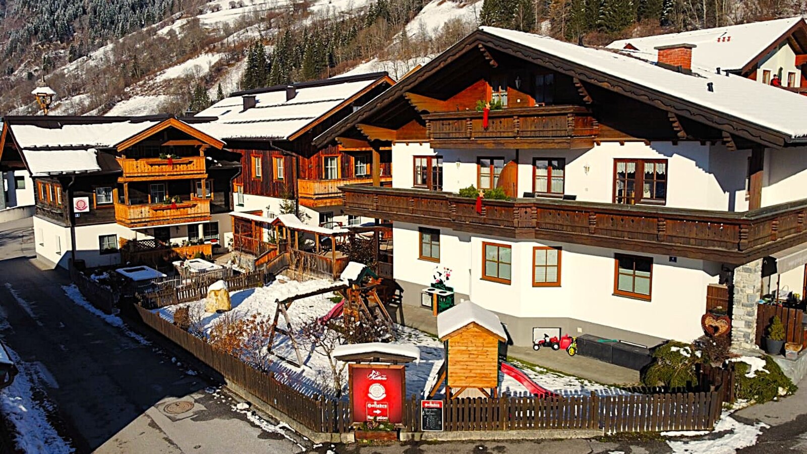 The Bauernhof buildings with balconies and a children's playground including a swing set and slide, set in the snow.