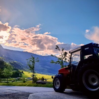 Tractor at the farmhouse with a mountain landscape in the background.