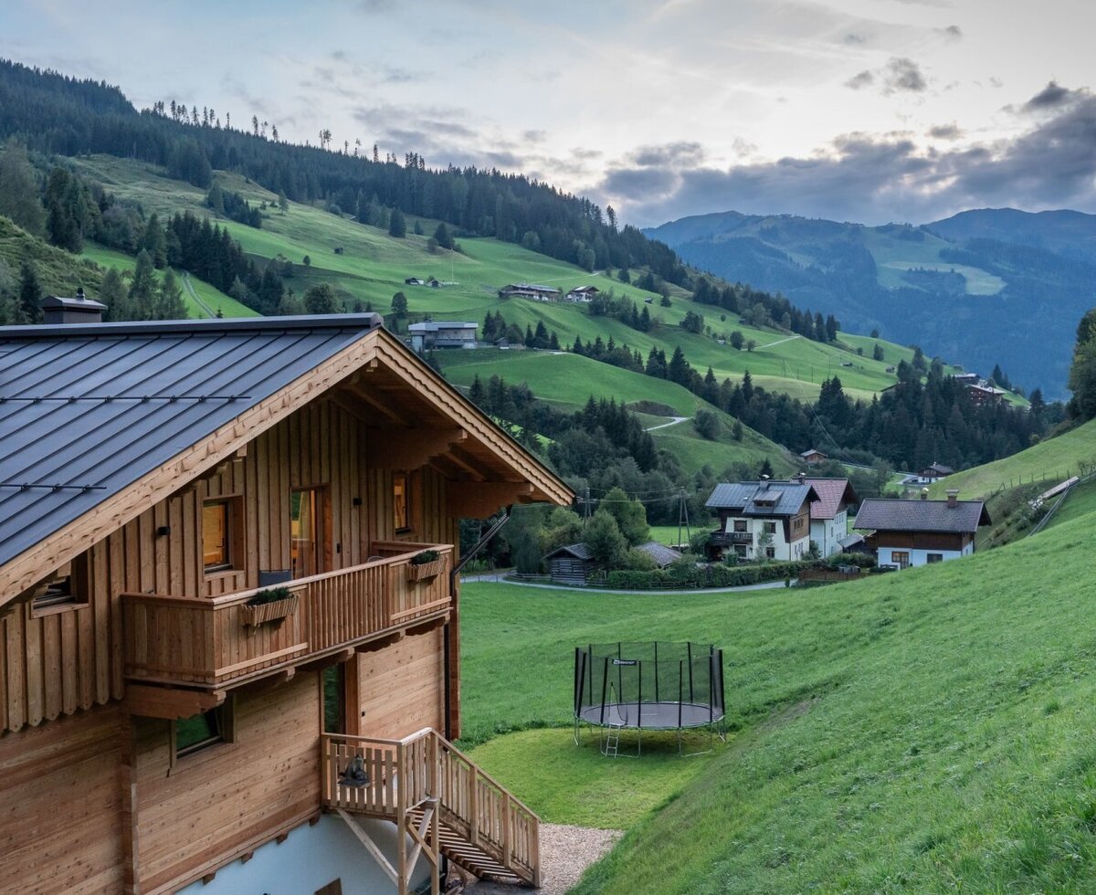 The farmstay is nestled in an idyllic mountain landscape featuring green meadows and a trampoline in the garden.