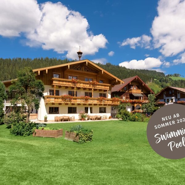 The two traditional farmhouses with balconies, set amidst a green lawn and mountain landscape.