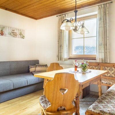 The farm house dining area features a traditional wooden table, corner bench seating, a sofa bed, and a window with mountain views.