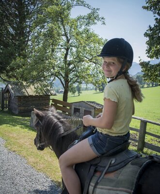Pony riding for children is available at the farm house, featuring a young rider wearing a helmet.