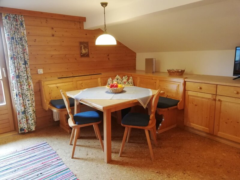 Farm House dining area with a wooden table, built-in corner benches, two chairs, and adjacent wooden storage cabinets.