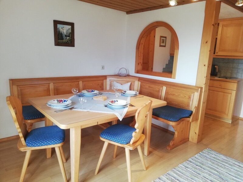 Dining area in the farm house featuring a wooden table, bench seating, chairs with blue cushions, and an adjacent compact kitchenette.