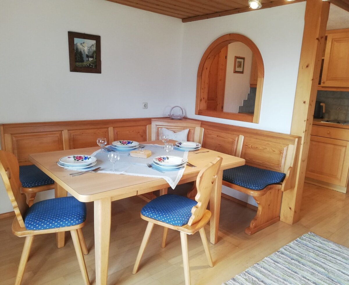 Dining area in the farm house featuring a wooden table, bench seating, chairs with blue cushions, and an adjacent compact kitchenette.