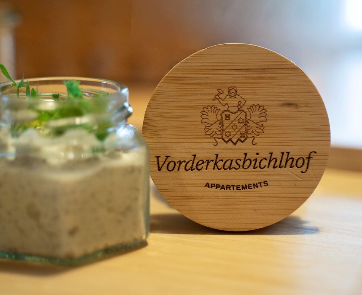 A small jar of creamy spread topped with fresh herbs, next to a branded wooden coaster from the Farm House.