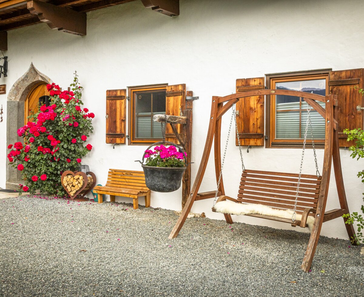 The farmhouse's inviting outdoor area featuring a cozy wooden swing, a bench, and vibrant climbing roses.