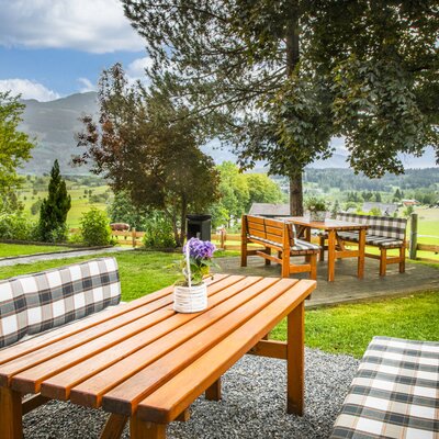 The farmhouse's inviting garden features cozy wooden seating areas shaded by mature trees.