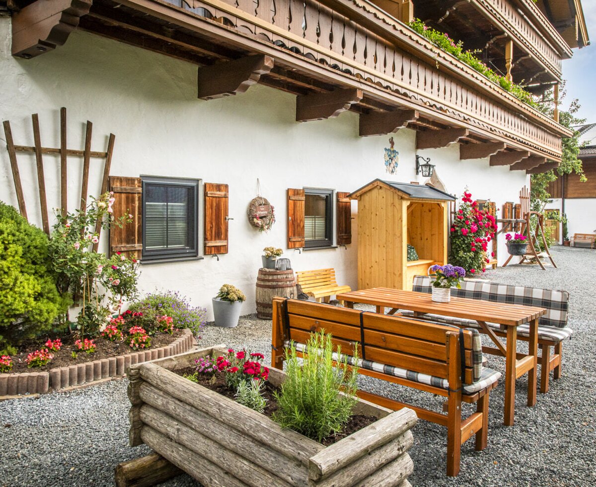 An inviting outdoor seating area at the farmhouse, featuring rustic wooden benches and colorful flower beds.