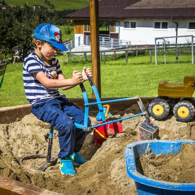 A sandpit at the Farm House, equipped with a toy excavator for children's play.