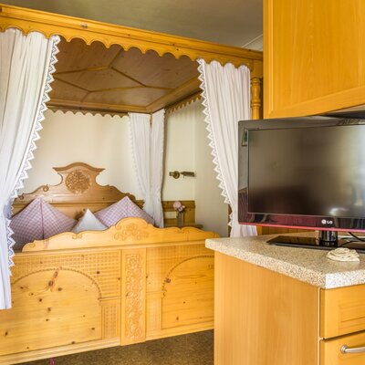 A bedroom in the Farm House includes a carved wooden four-poster bed and a flat-screen TV on a storage cabinet.