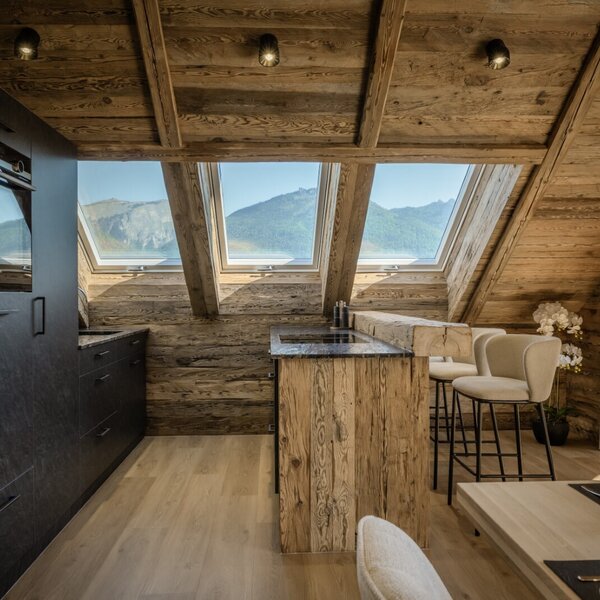 The Farm House offers a modern kitchen with black cabinetry and an integrated oven, a wooden island bar, and skylight windows providing mountain views.