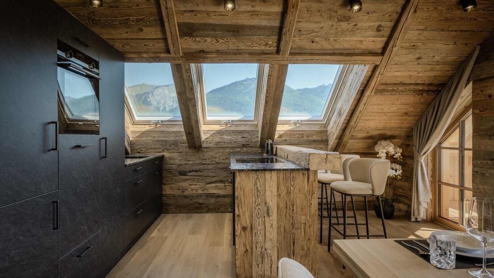 The Farm House offers a modern kitchen with black cabinetry and an integrated oven, a wooden island bar, and skylight windows providing mountain views.