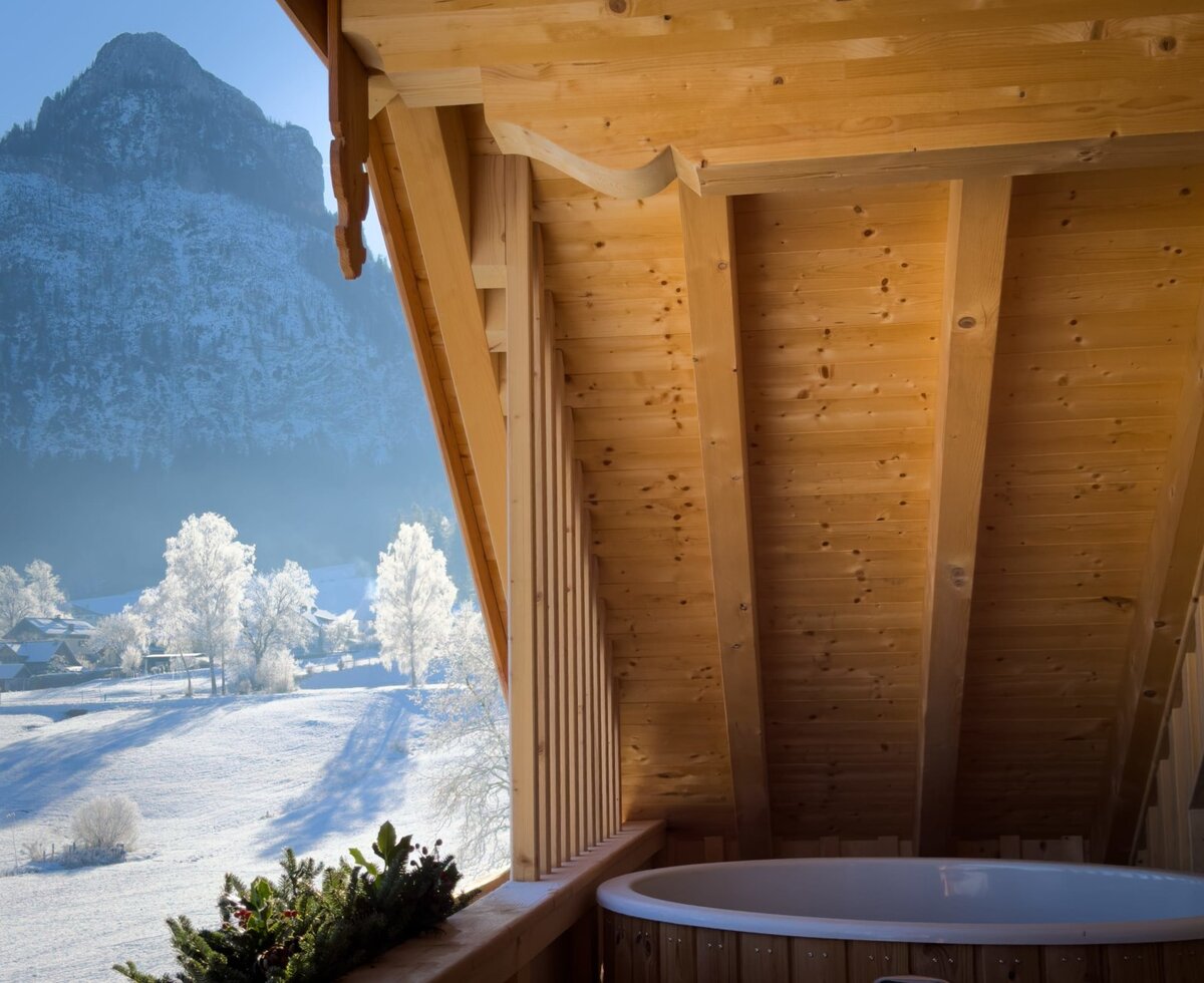 Balcony at the Farm House with an outdoor hot tub, offering a view of the snow-covered mountains and winter landscape.