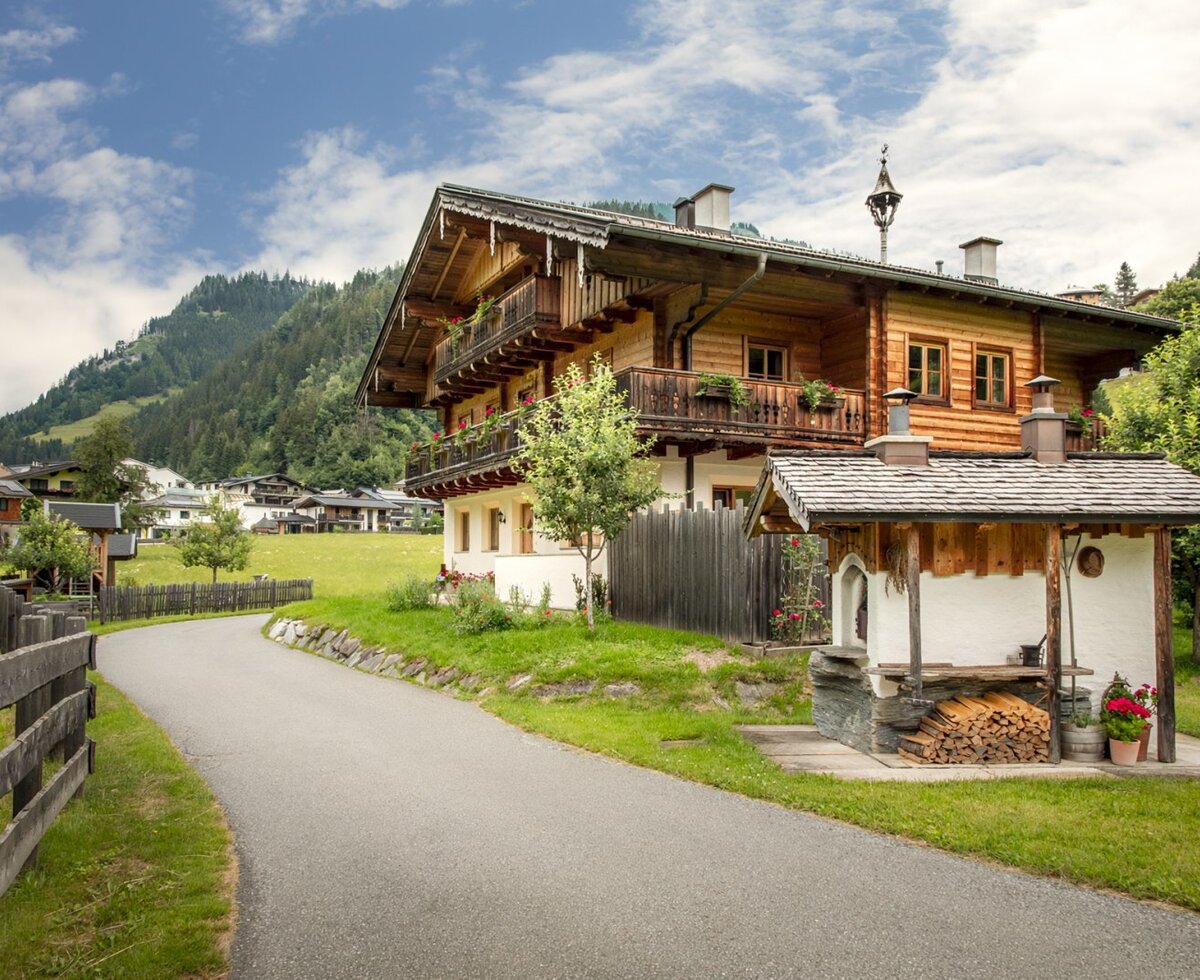 A traditional wooden farmhouse with flower-adorned balconies and a charming outdoor bread oven in the green garden.