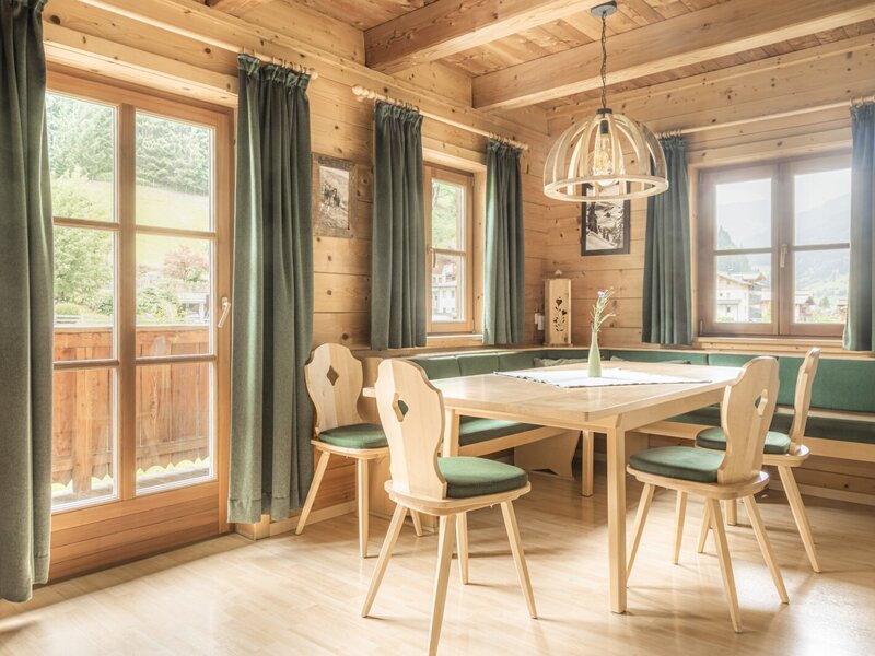 A cozy dining area in the farmhouse with a rustic wooden corner bench, matching chairs, and bright natural light.