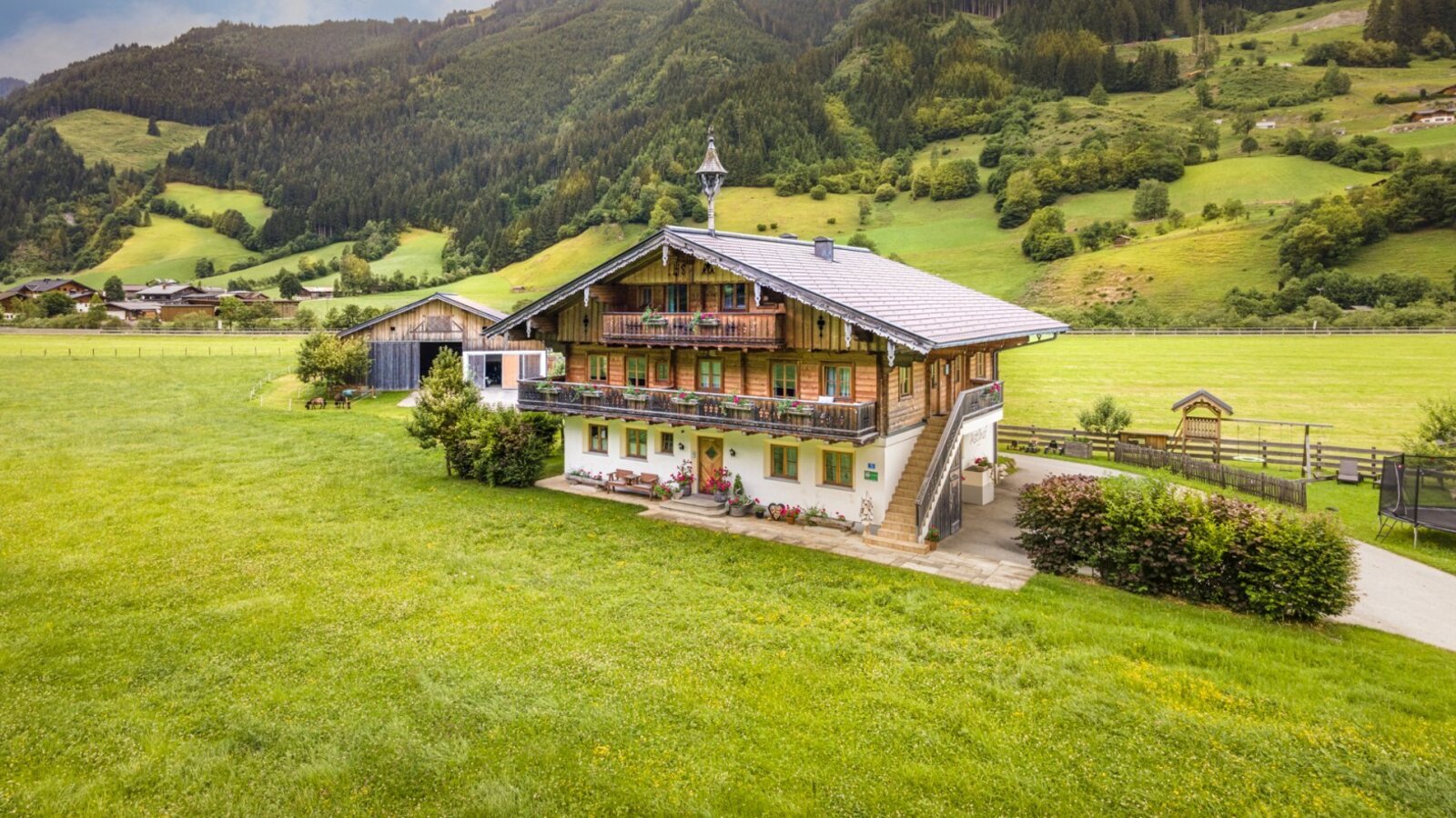 The inviting farmhouse surrounded by lush green meadows and a scenic mountain backdrop.