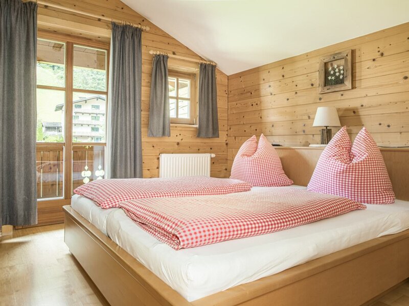 A cozy double room in the farmhouse featuring wood-paneled walls, classic red-and-white checkered bedding, and balcony access.