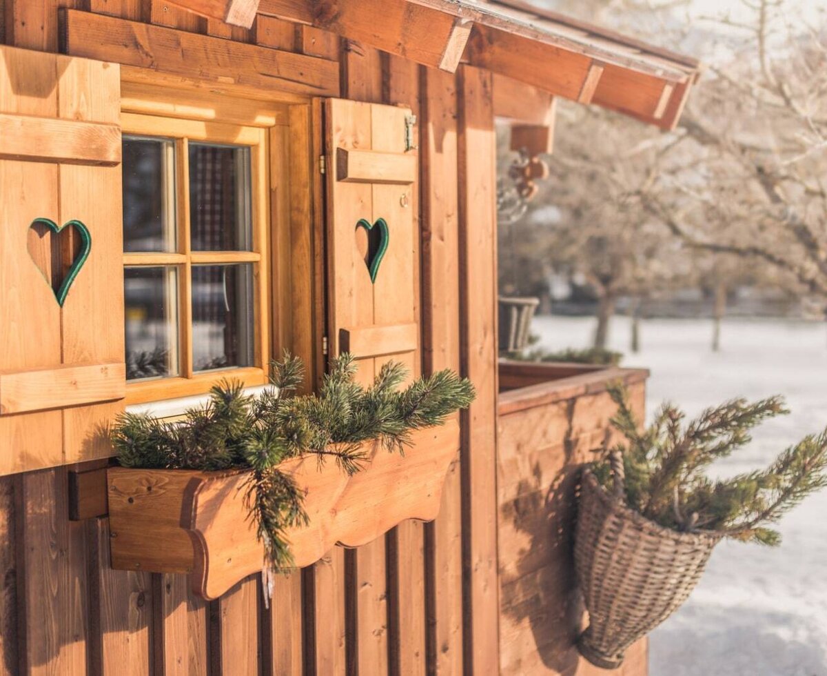 A window of the Ap­par­te­ments, featuring wooden shutters with a heart cutout and a window box with pine branches.