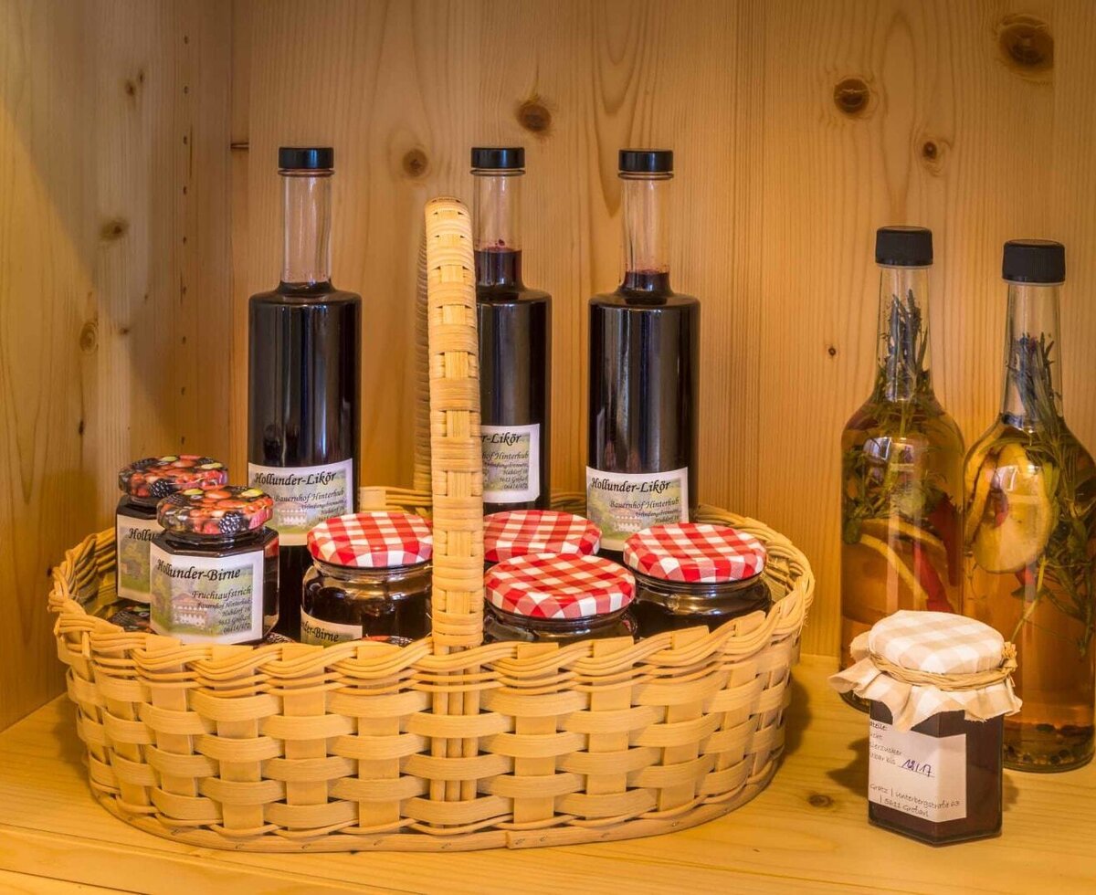 An inviting wicker basket inside the farmhouse's wooden cabinet, filled with homemade liqueurs and jams with classic red-and-white checkered lids.