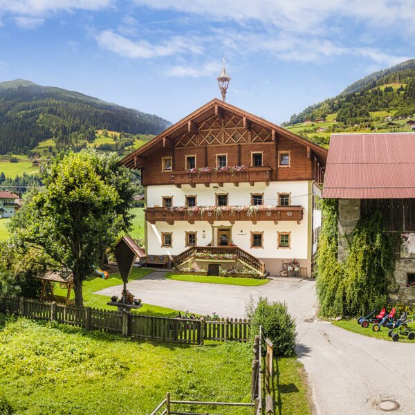 The inviting farmhouse features traditional alpine architecture, surrounded by a spacious green lawn and beautiful mountain slopes.