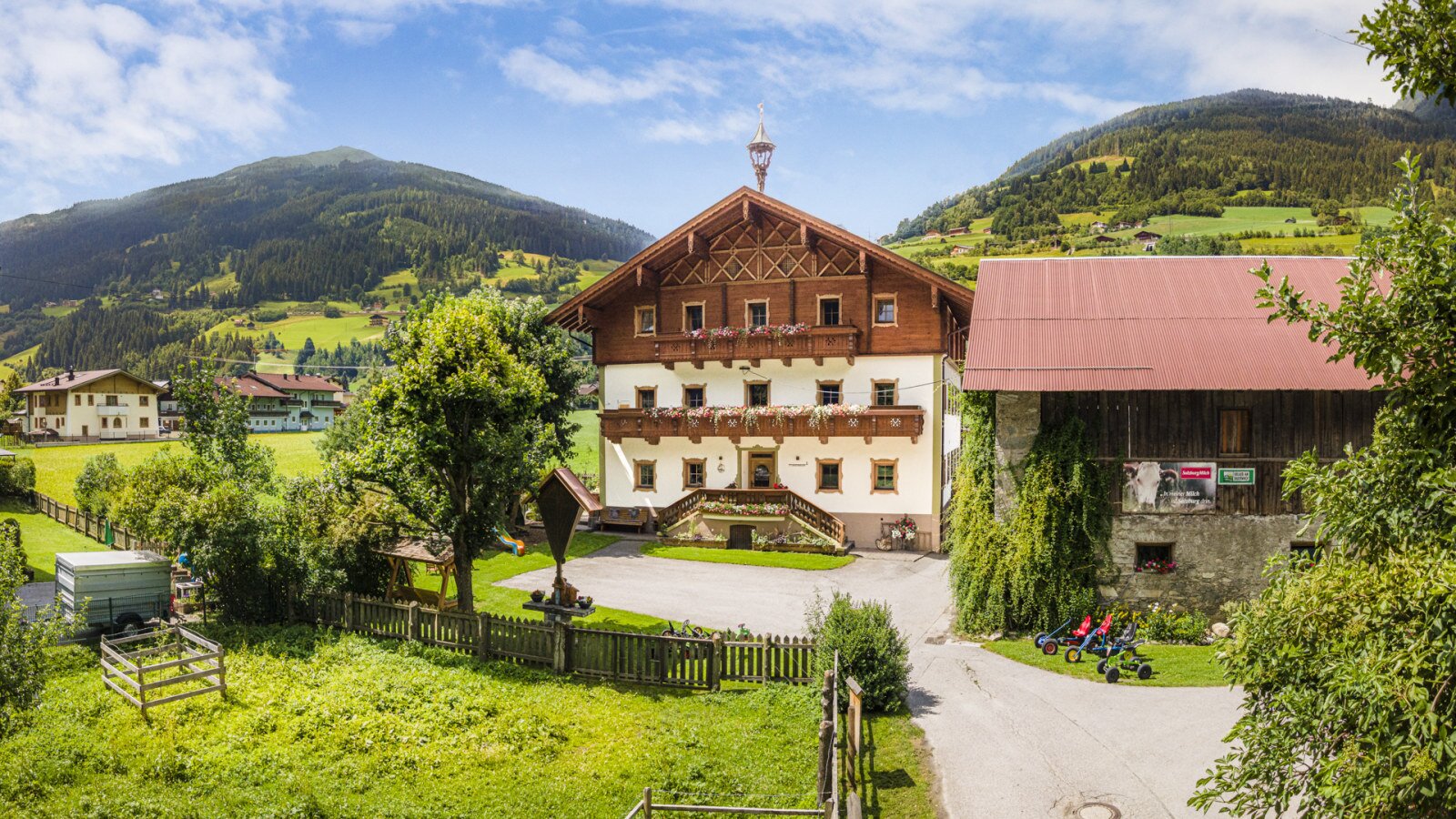 The inviting farmhouse features traditional alpine architecture, surrounded by a spacious green lawn and beautiful mountain slopes.