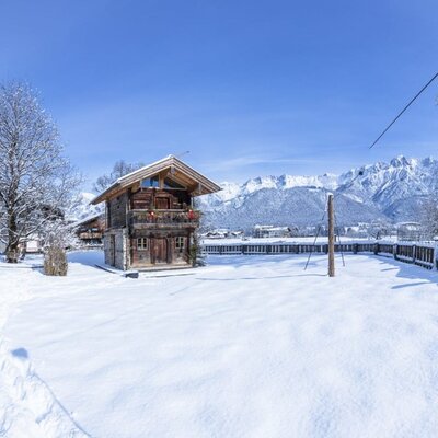 Winter landscape of the farmhouse with snow-covered buildings and mountains in the background.