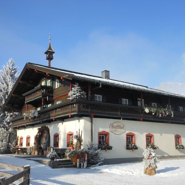 The Farm House exterior during winter, featuring snow-covered grounds, traditional balconies, and frosted trees.
